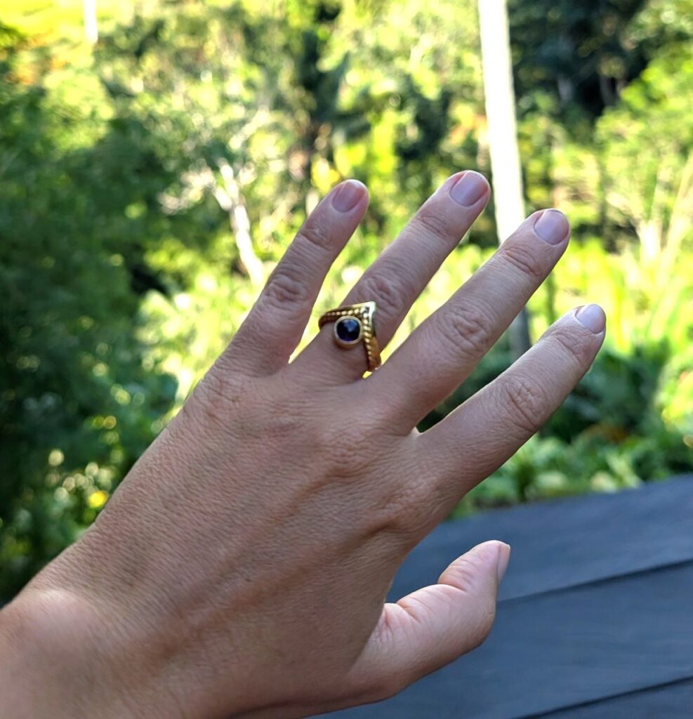 La bague dorée avec pierre violette fabriquée à l'Alam Ubud Jewelry Workshop portée au doigt devant la nature d'Ubud Bali