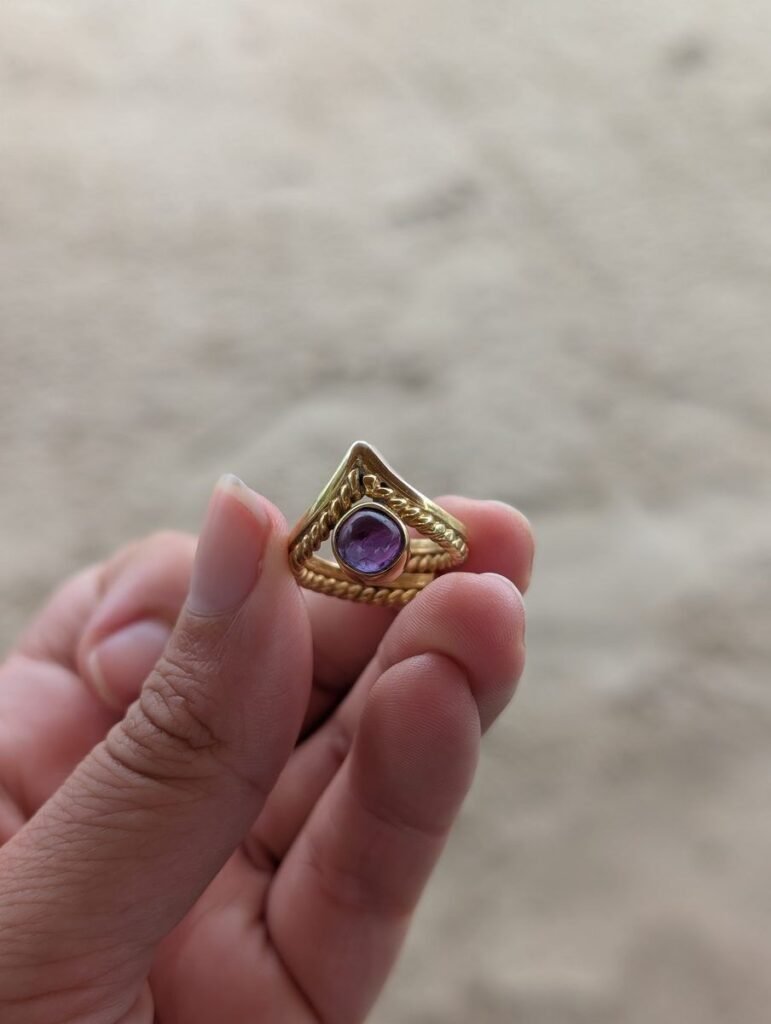 Bague dorée avec pierre violette fabriquée à l'Alam Ubud Jewelry Workshop tenue dans la main à Bali